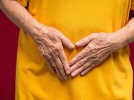 Close-up of hands senior woman touching belly because suffering from abdominal pain while standing on a red background photo