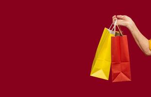 Close-up of hand holding yellow and red shopping bags with a handle while standing on a red background photo