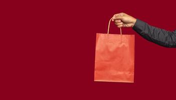 Hand holding a red paper bag with a handle while standing on a red background photo