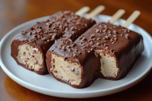 Chocolate covered ice cream bars with chocolate sprinkles resting on white plate photo