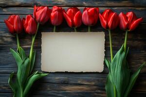 Row of red tulips framing old paper on rustic wooden background photo