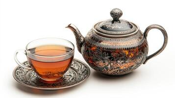 Elegant teapot pouring tea into glass cup on ornate saucer photo
