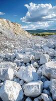 White limestone rocks are covering the slope of a quarry under blue sky with cumulus clouds photo