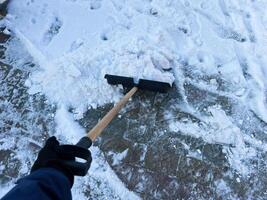 Person shoveling snow from a winter sidewalk with a manual snow shovel photo