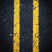 Close-up view of peeling yellow road markings on a black asphalt surface during daylight photo