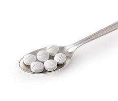 Different types of white pills are resting on a spoon in a clinical setting photo