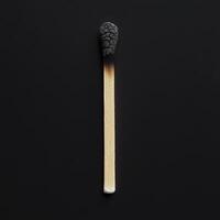 Burned matchstick lies on a black surface showcasing its charred head and wooden shaft illuminated by soft light photo