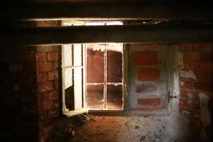 Walled basement window with broken panes and some daylight falling in photo