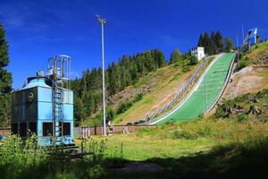 Ski jump structure in green hillside surrounded by trees under blue sky in Oberhof, Germany photo