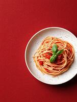 Overhead view of a plate of spaghetti with tomato sauce and basil on a red background photo