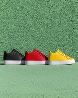 Three stylish sneakers in black, red, and yellow against a green wall photo