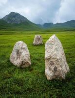 Three stones in a field with mountains in the background photo
