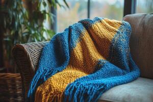 Cozy blue and yellow crocheted blanket draped over a vintage armchair in a warm living room setting photo