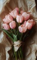 Beautiful bouquet of pink tulips wrapped in kraft paper on rustic wooden table photo