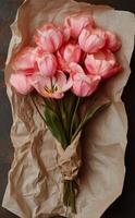 Beautiful bouquet of pink tulips wrapped in kraft paper on rustic wooden table photo