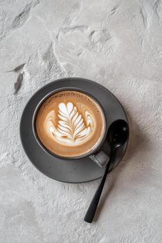 Beautiful latte art in a textured gray cup served on a matching saucer with a small spoon photo