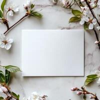 Blank card surrounded by delicate pink flowers and green leaves on rustic wooden background photo