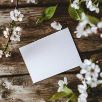Blank card surrounded by delicate pink flowers and green leaves on rustic wooden background photo