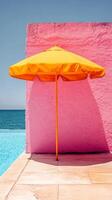 Bright yellow umbrella beside a serene swimming pool against a pink wall photo