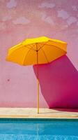 Bright yellow umbrella beside a serene swimming pool against a pink wall photo