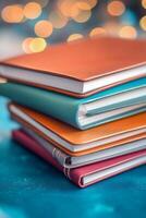 Colorful stacked notebooks on blue surface with sparkling lights in the background during evening hours photo