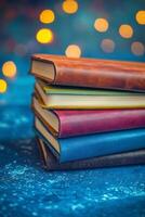 Colorful stacked notebooks on blue surface with sparkling lights in the background during evening hours photo