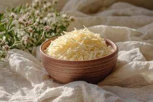 A minimalistic presentation of shredded cheese in a small ceramic bowl, placed on a plain linen cloth photo