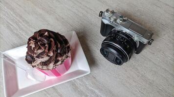 Mirrorless camera in retro style and cake or croissant on wooden table. photo