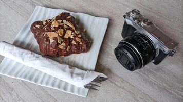 Mirrorless camera in retro style and cake or croissant on wooden table. photo