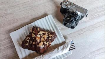 Mirrorless camera in retro style and cake or croissant on wooden table. photo