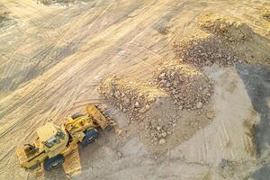 aerial drone top view. a bulldozer with piles of soil at a construction site. A construction site with large yellow machine. The machines are digging into the sand. The sand is piled up in a mounds photo