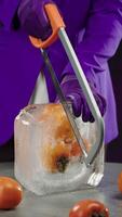 Chef in a purple jacket uses a hacksaw to saw frozen persimmons in an ice cube video