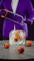 Chef in a purple jacket uses a hacksaw to saw frozen persimmons in an ice cube video