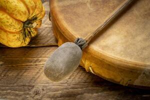handmade, native American style, shaman frame drum covered by goat skin with a beater on a rustic wood with winter squash photo