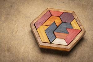 wooden hexagon tangram puzzle against textured handmade bark paper, brain teaser and fun game with multiple ways to solve photo