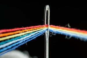 multi-colored threads for sewing in the form of a rainbow pass through an antique needle on a black background photo