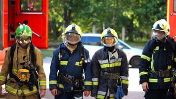 Portrait of male and female firefighters in helmets and protective uniforms standing near big red car. Young confident fireman and firewoman in full equipment posing against background of fire engine photo