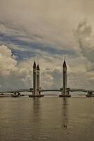 A stunning photogenic Kuala Terengganu drawbridge under a dramatic cloudy sky with structure featuring twin towers and a modern design that nestled against the ocean below. photo