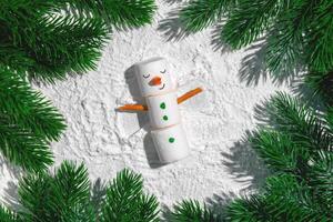 Funny marshmallow snowman lying on snow, creating a snow angel with pretzel stick arms, capturing the playful spirit of winter holidays and festive celebrations photo