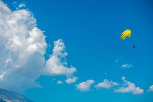 Two people parasailing on a yellow parachute flying against the background of mountains, blue sky and clouds photo