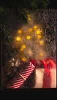 Christmas tree with yellow lights is visible through frosted window with ice patterns and christmas gifts wrapped in striped and red paper are lying near the window photo