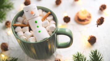 cute christmas card, Cheerful marshmallow snowman relaxes in a green mug of hot chocolate, surrounded by mini marshmallows, cinnamon sticks, and festive christmas lights, creating cozy holiday scene photo