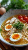Close-up of a bowl of chicken noodle soup with egg and tomato photo