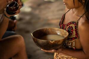 Wayuri indigenous girl offering a bowl of Chicha drink to a tourist in Ecuadorian Amazon photo