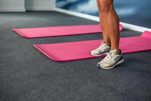 copyspace Closeup of elderly athlete's legs next to two pink yoga mats on gym floor during class photo
