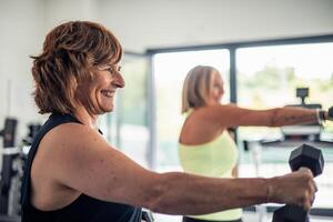 Closeup of elderly woman smiling doing arm exercises with dumbbells during fitness class in the gym photo