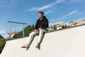 Low-angle shot of skater resting at skate park, focused while sitting on half-pipe edge photo