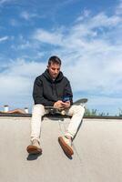 vertical Skater enjoying a break while texting on smartphone at half-pipe edge photo