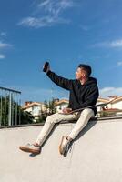 vertical Skater enjoying a fun selfie moment with smartphone at the half-pipe in skate park photo