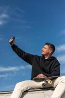 Vertical low-angle shot of a smiling skater taking a selfie with smartphone in skate park photo